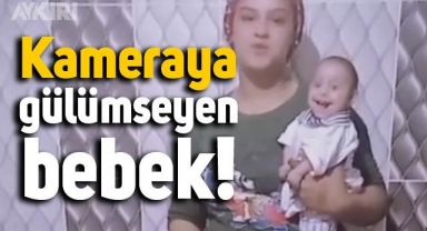 Çok küçük olmasına rağmen önündeki kameraya gülümseyen bebek